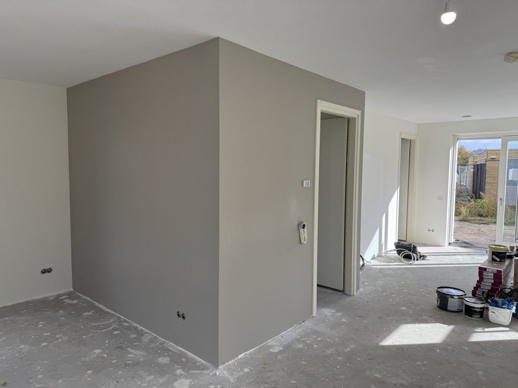 Pas gesausde wand in een warme grijze kleur in een nieuwbouwwoning, met verfemmers bij de tuindeuren