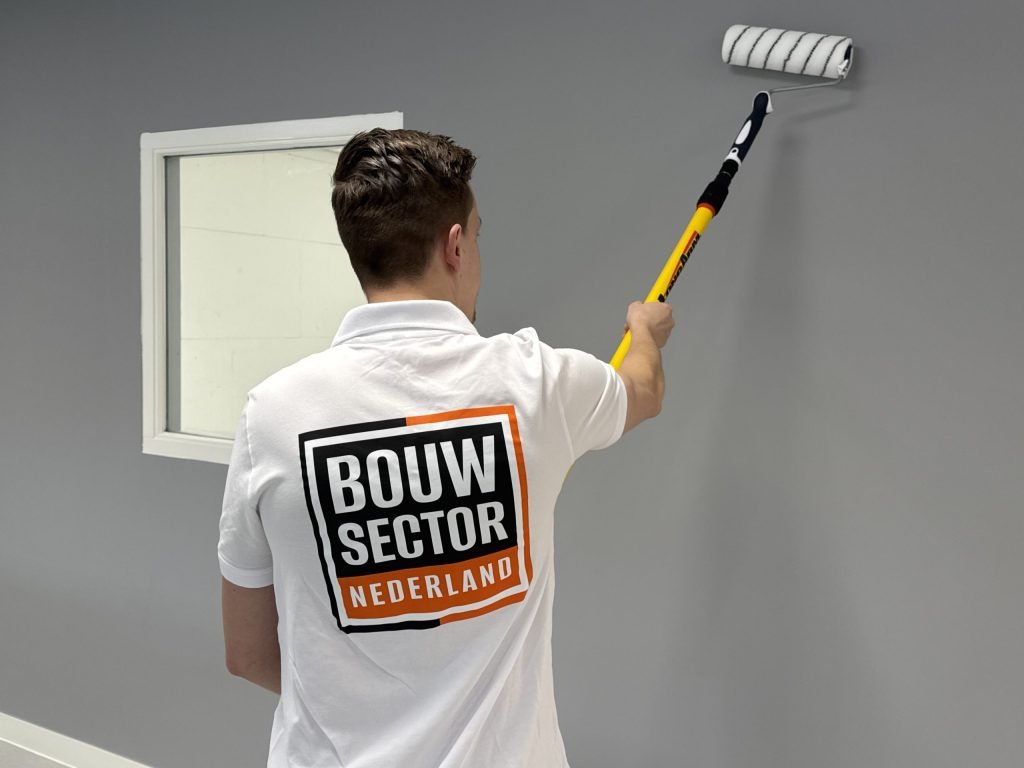 Schilder van Bouwsector Nederland rolt een grijze muur naast een wit binnenraam