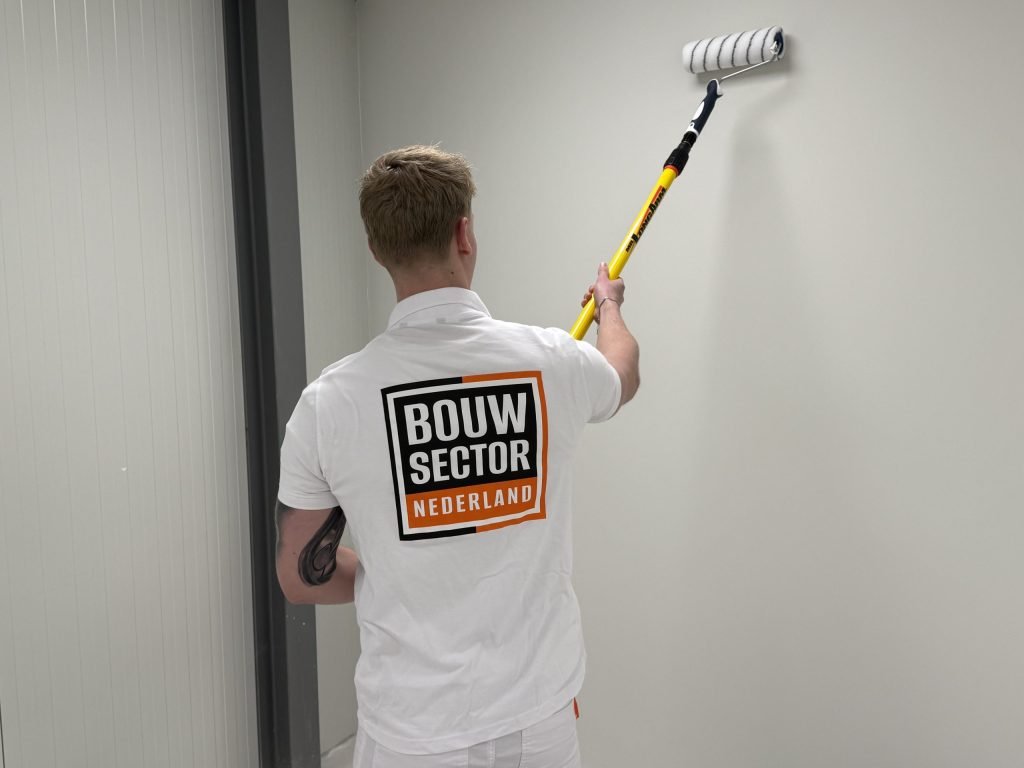 Schilder van Bouwsector Nederland rolt een lichte wand in een gang met een roller op een verlengsteel