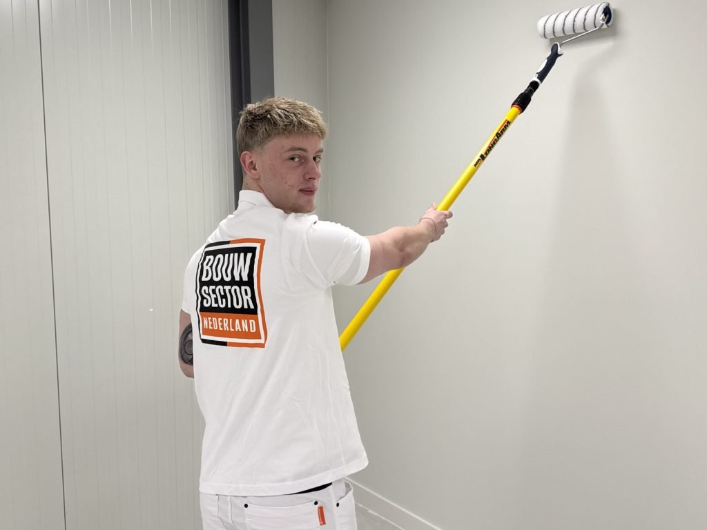 Schilder van Bouwsector Nederland kijkt om terwijl hij een lichte wand in een gang rolt